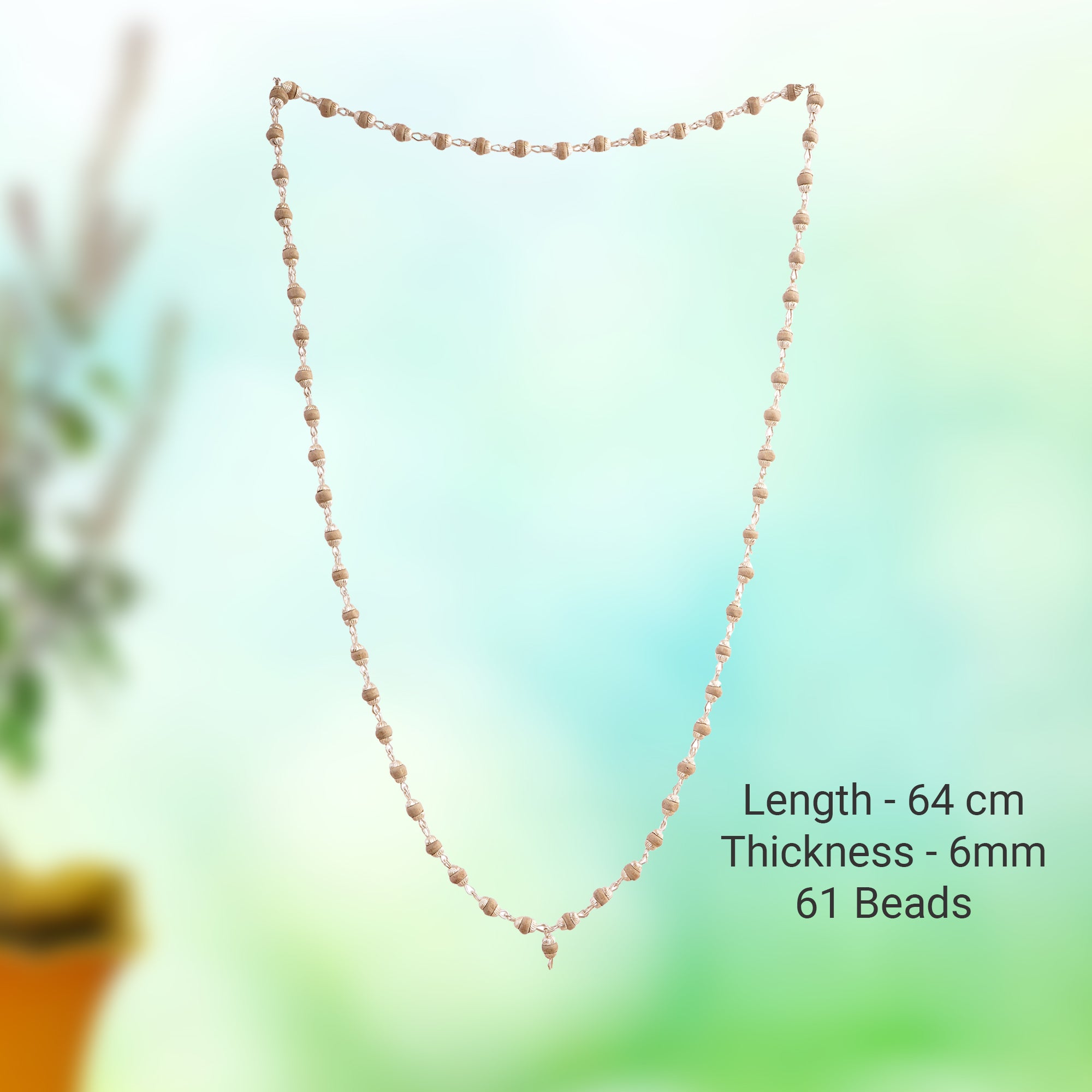 A beaded necklace with small, round, light pinkish-beige beads arranged in a shield shape against a soft, blurred green and blue background. Text on the right specifies the product details: 'Length - 64 cm, Thickness - 6mm, 61 Beads'.